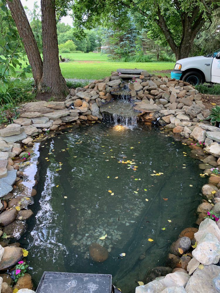 A pond with a waterfall and a truck parked in the background.