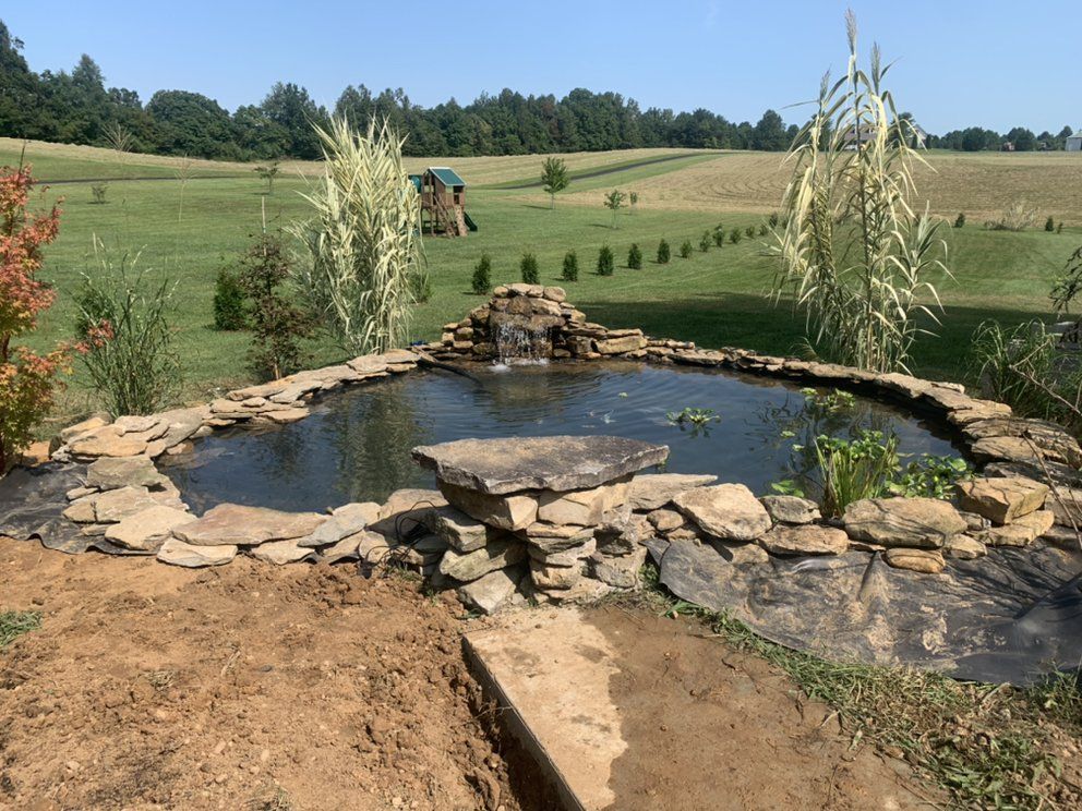 A pond with a waterfall in the middle of a field.