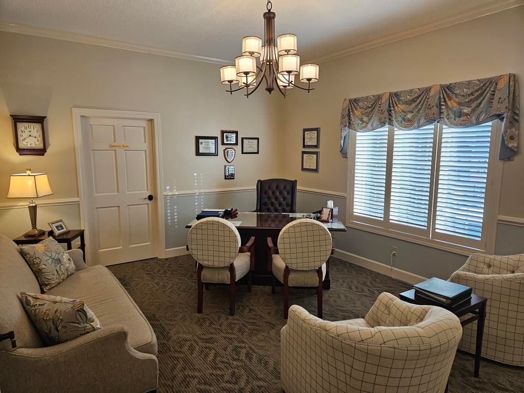 A well-lit office with desk, chairs, sofa, and window with a chandelier overhead.