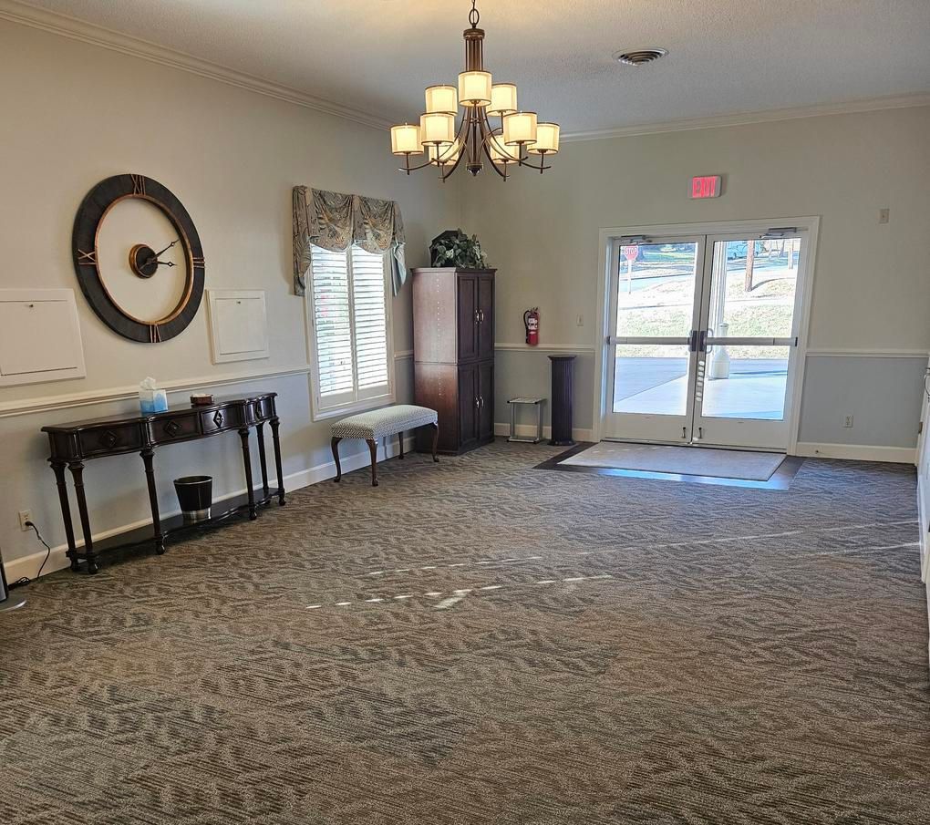 Empty room with carpet, double doors, and chandelier. Features a console table, clock, cabinet, and bench.