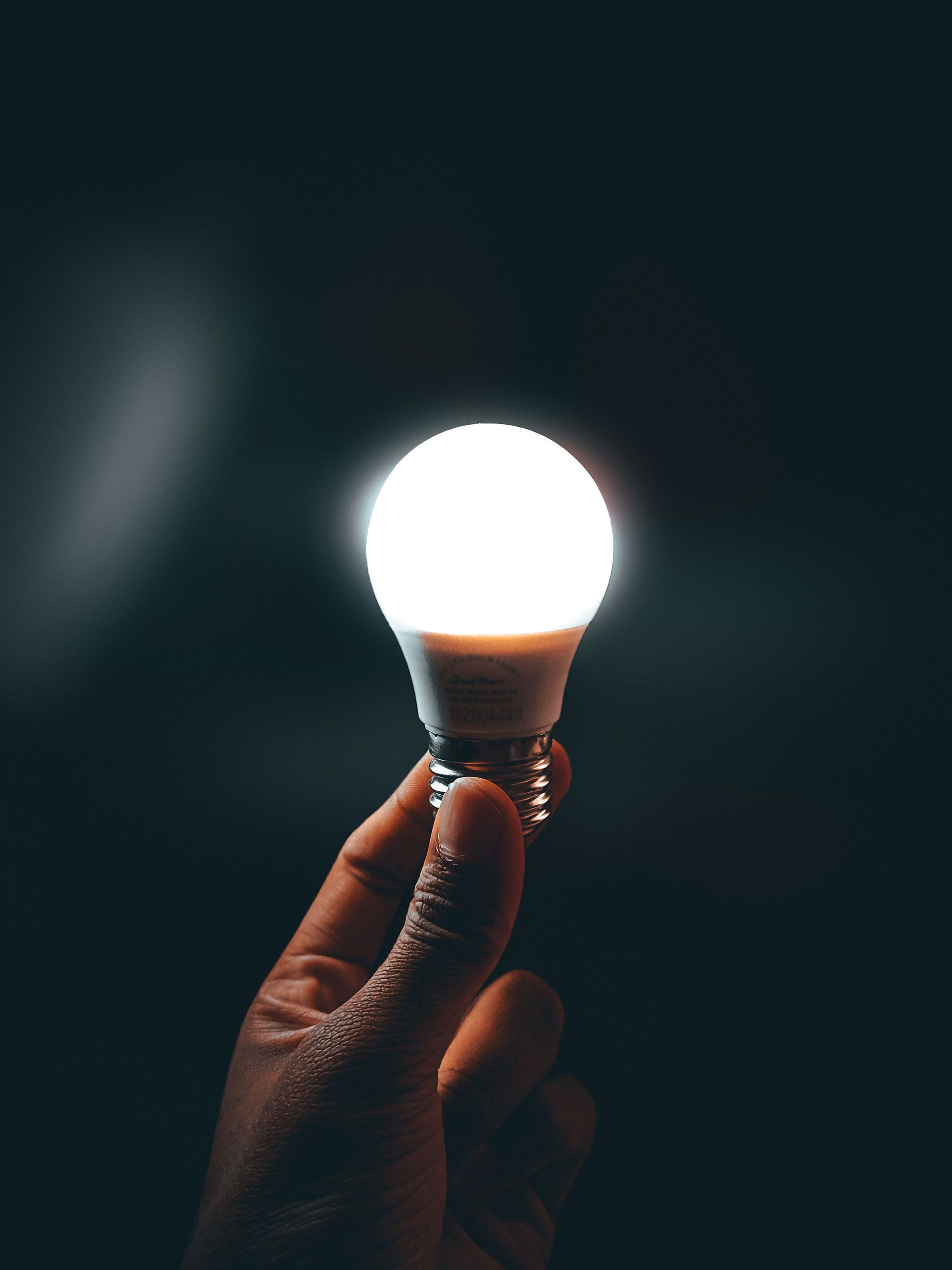 Hand holding a glowing lightbulb against a dark background, symbolizing an idea or innovation.