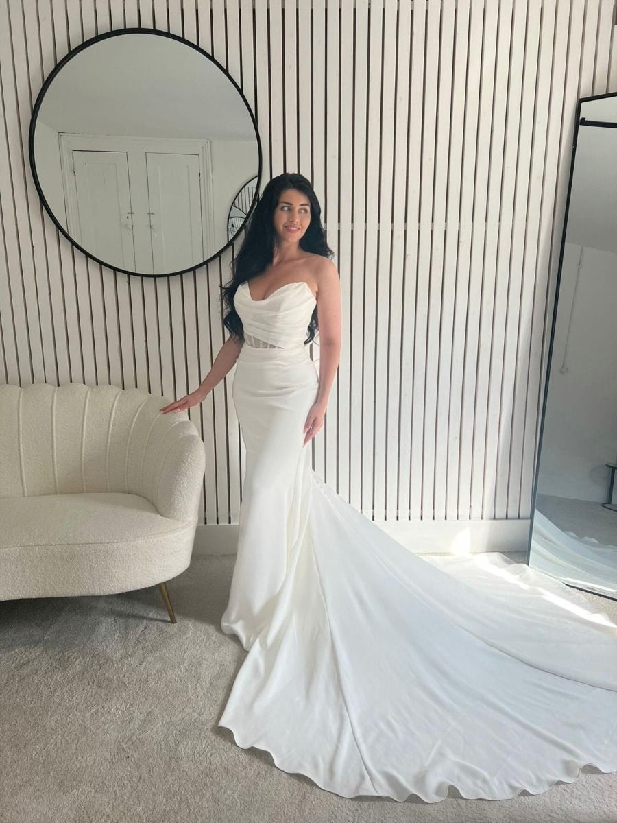 Lady stood in a modern, timeless, Ivory wedding dress by TWH Couture. The wedding dress has a prominent sweetheart neckline with a panel going across to made it modest, a sheer illusion cut out bodice panel with exposed boning and pleating on the bodice and skirt.