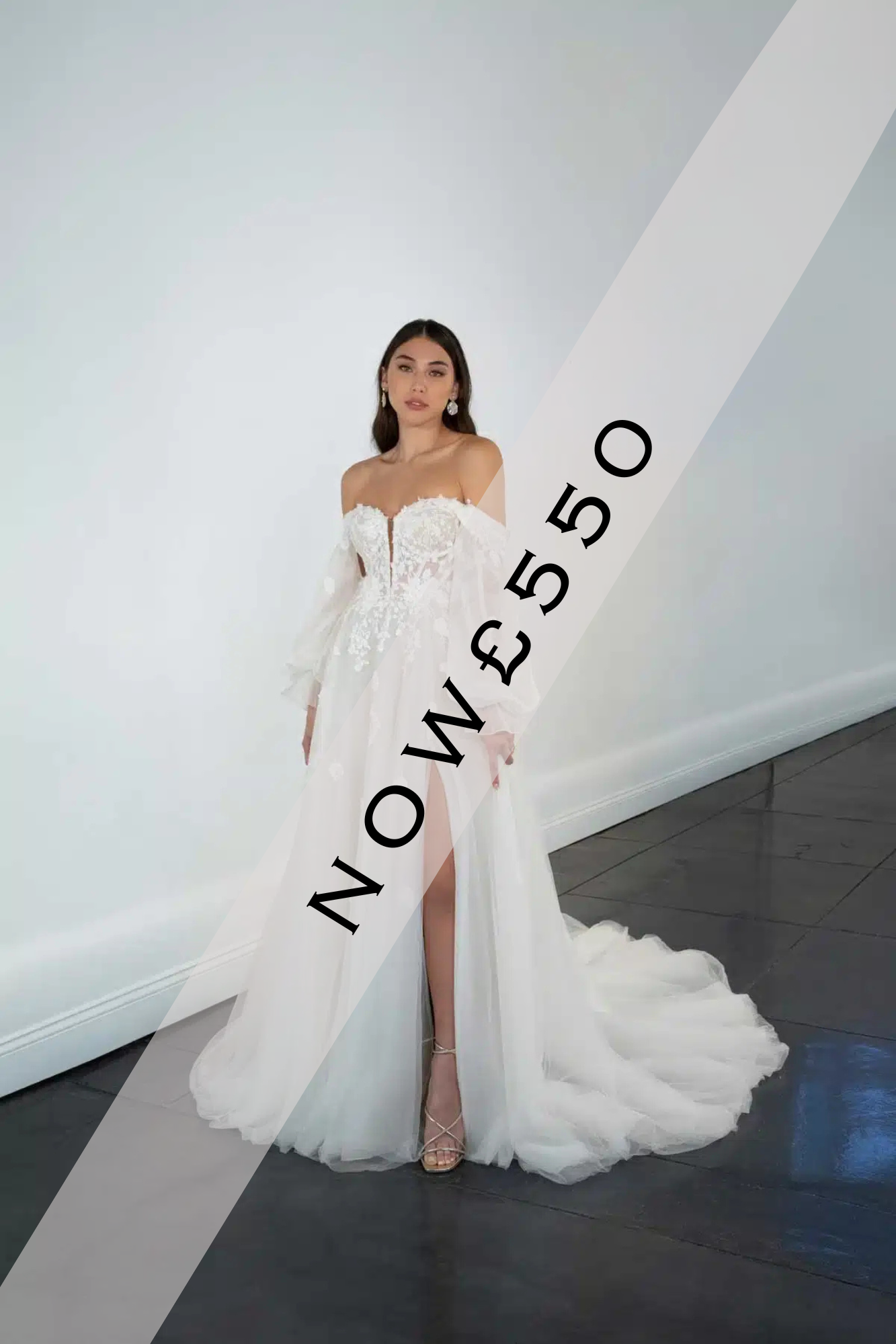 Lady stood holding flowers in a Sweetheart neckline, a-line wedding dress by Martina Liana. The wedding dress has a leg split, floaty tulle skirt, exposed boning, illusion bodice and lace detail on the bodice that gently flows on to the skirt of the dress. The sleeves are floaty and off the shoulder with floral lace detailing.