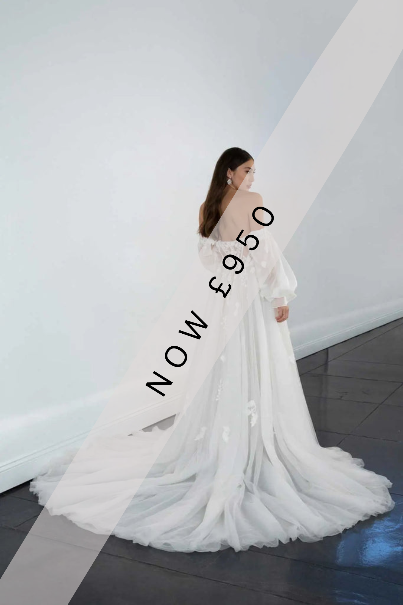 Lady stood in an Ivory/Rum wedding dress by Martina Liana. The wedding dress has a floaty tulle overlay with floral lace motifs and a rum lining. It also has a sheer illusion tulle back with a zip and buttons.