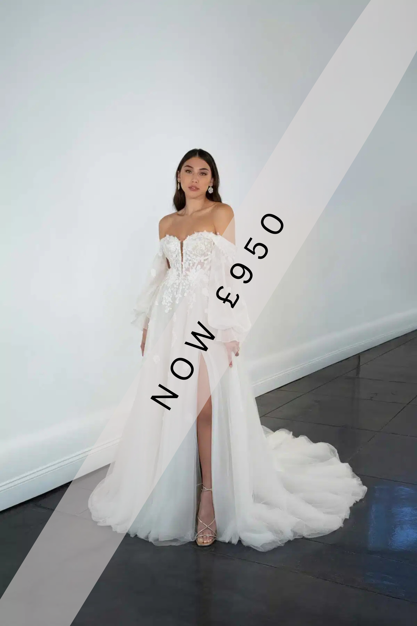 Lady stood holding flowers in a Sweetheart neckline, a-line wedding dress by Martina Liana. The wedding dress has a leg split, floaty tulle skirt, exposed boning, illusion bodice and lace detail on the bodice that gently flows on to the skirt of the dress. The sleeves are floaty and off the shoulder with floral lace detailing.