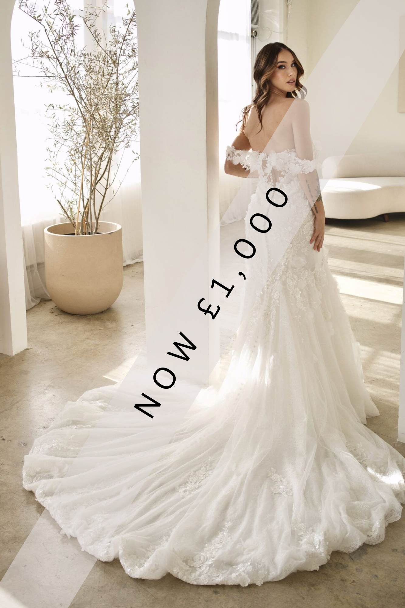 Lady stood in Martina Liana wedding dress with illusion back, 3D floral off the shoulder straps. The back of the wedding dress is detailed with a zip, buttons and floral lace detail throughout the bodice, skirt and train.