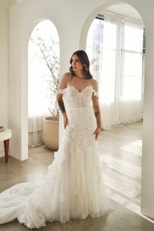 Lady stood in Ivory, lace, fishtail wedding dress. The wedding dress has soft 3D floral lace off the shoulder straps, 3D floral lace on the bodice that drops down onto the top of the skirt.