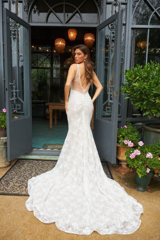 Lady stood in soft delicate lace and bead Ivory wedding dress by Martina Liana. It has a low tulle illusion back, pleating over the bum and button detailing.