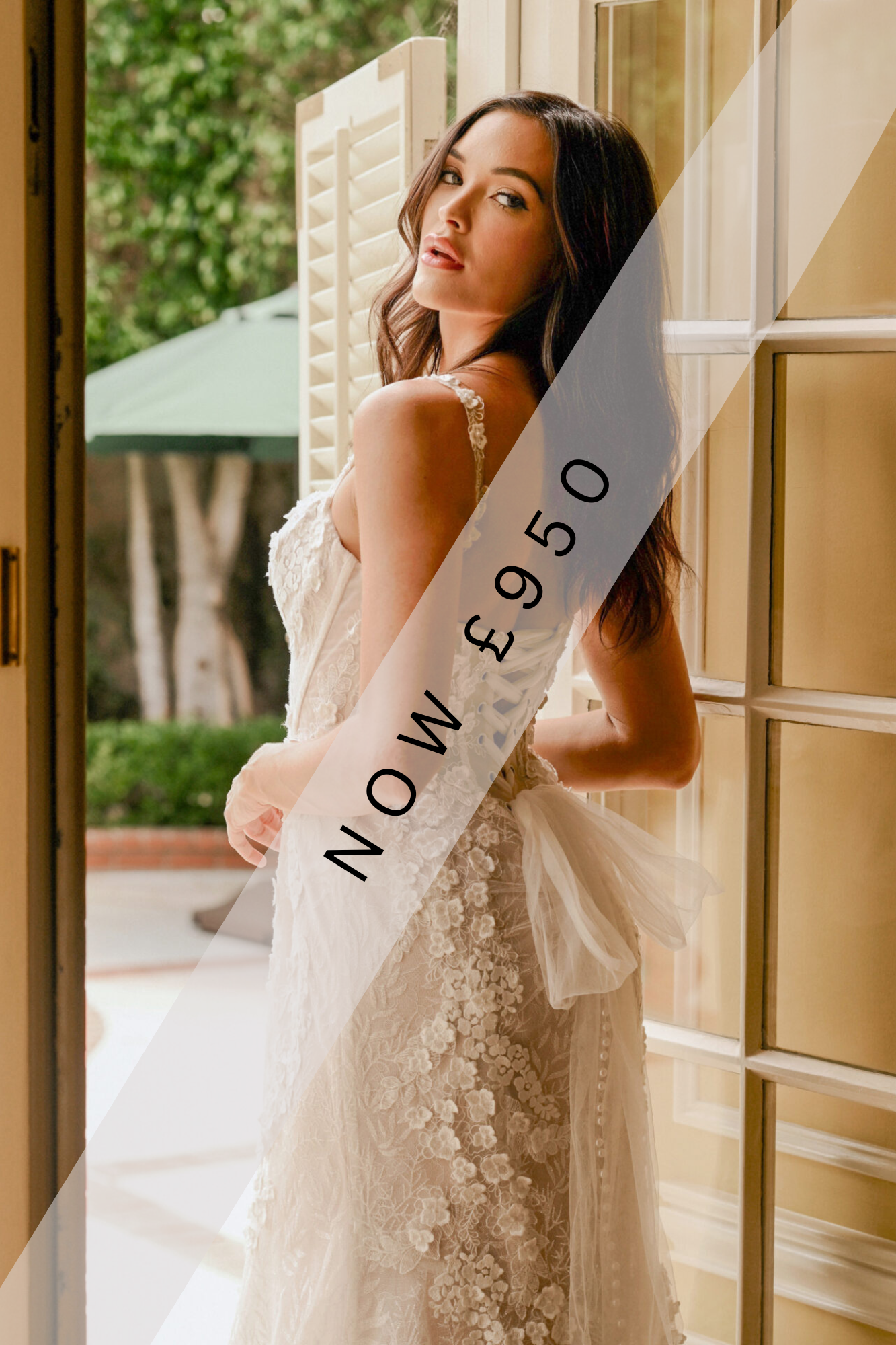 Lady stood in lace detailed, Ivory wedding dress by Martina Liana. The wedding dress has lace motif going down the back, corset back and buttons all down the back of the wedding dress.