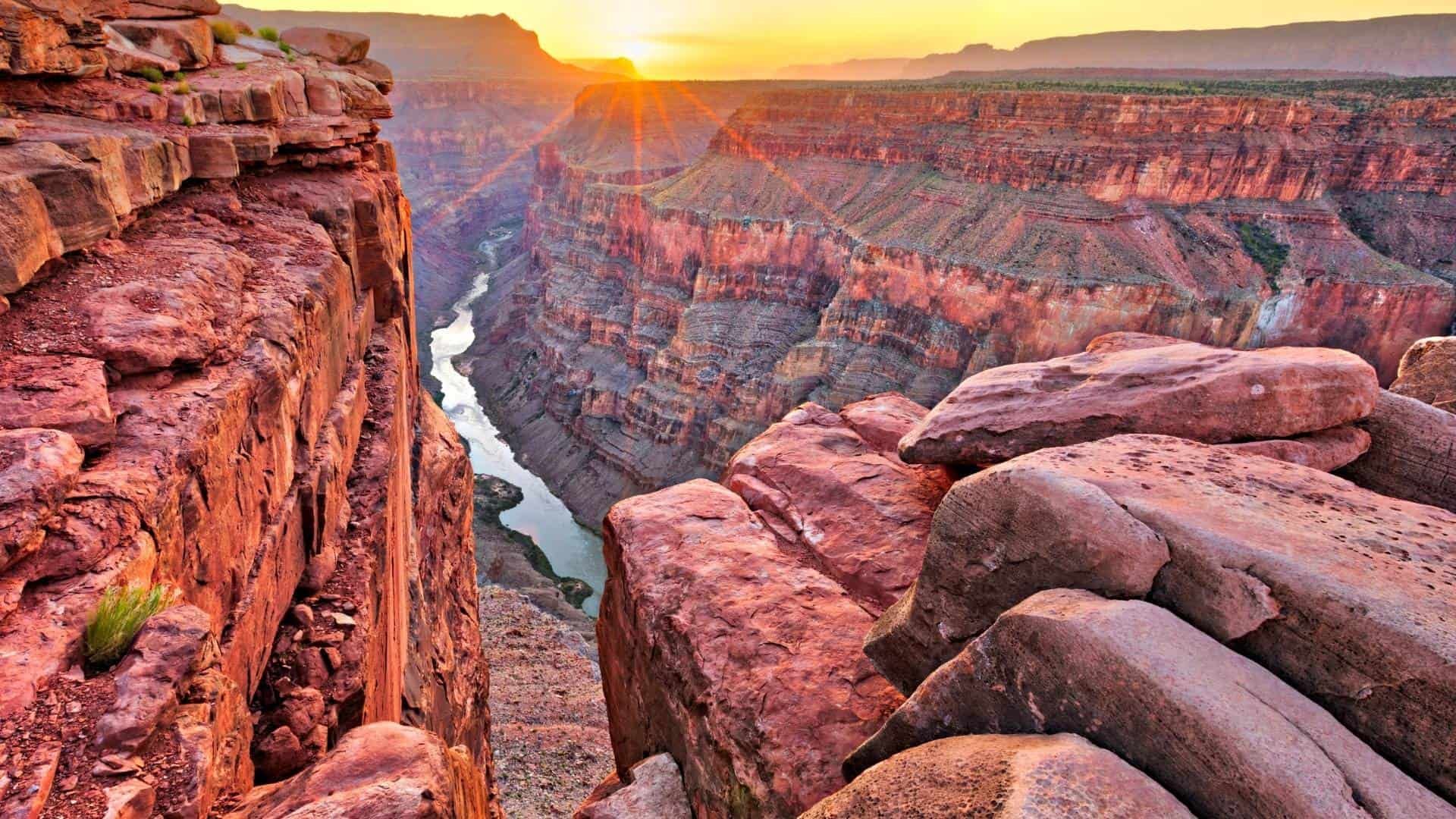 The sun is setting over a canyon with a river running through it.
