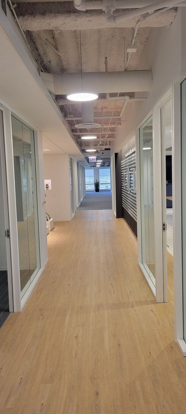 A long hallway in an office building with wooden floors and glass doors.