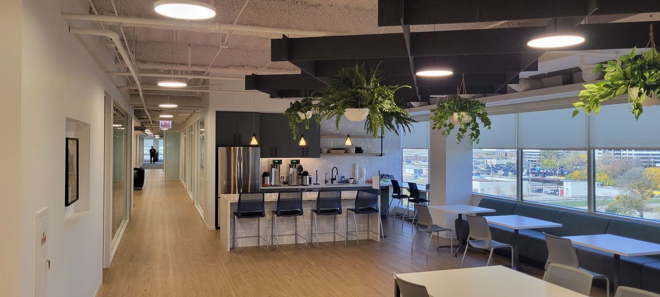 A long hallway in an office building with tables and chairs and plants hanging from the ceiling.