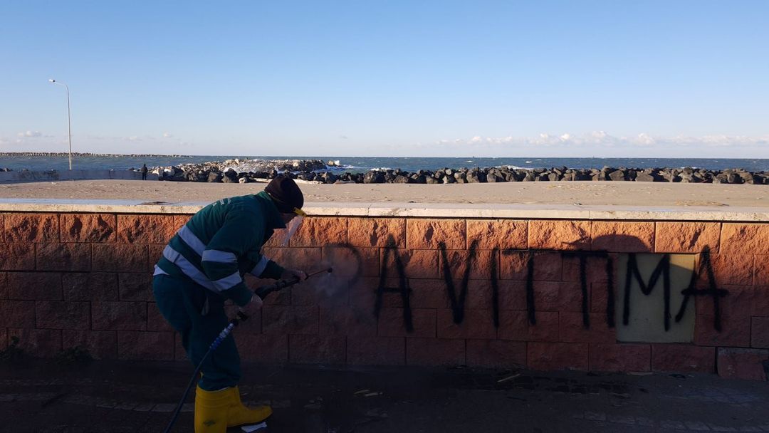 Un operaio con indosso una tuta da lavoro verde utilizza un'idropulitrice per rimuovere la scritta 