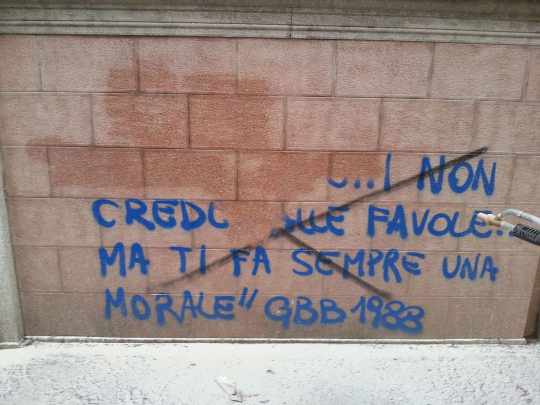 Blue graffiti on a brick wall reads, 