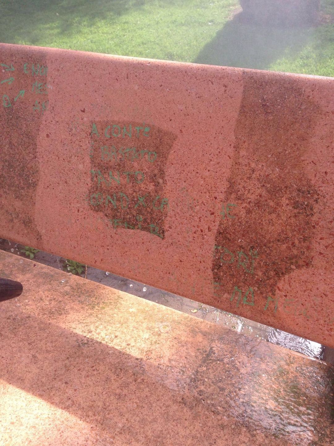 Una panchina in pietra rossa con macchie scure e umide causate dalla pioggia recente.