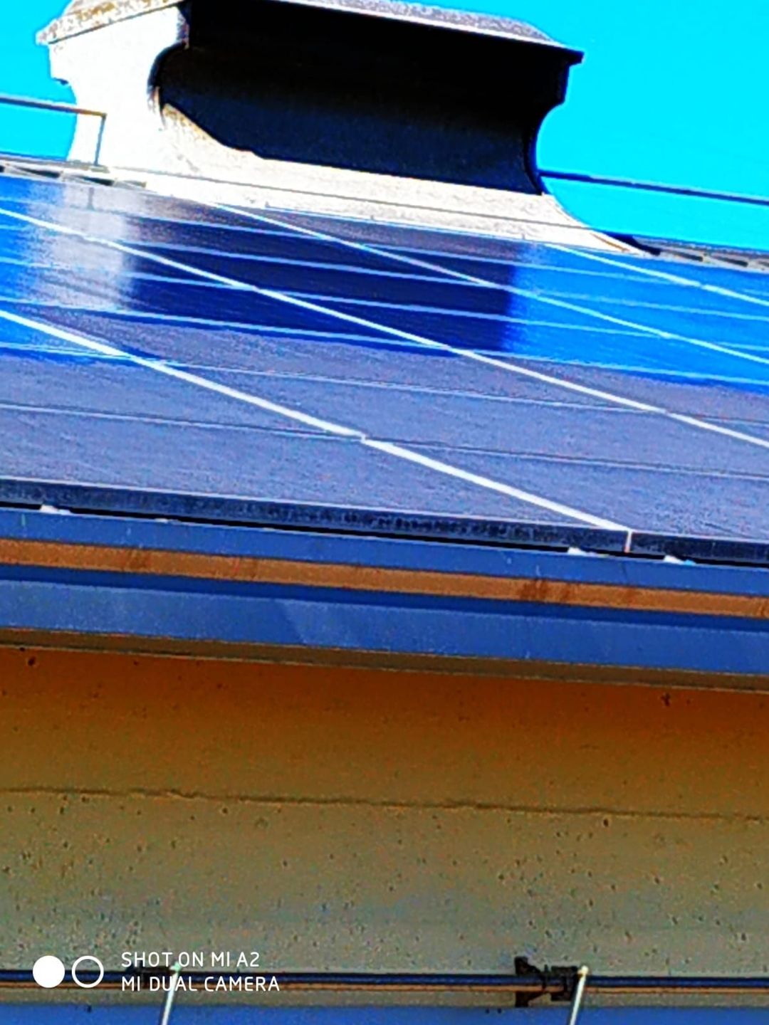 Pannelli solari installati su un tetto sotto un cielo azzurro brillante, con un camino visibile sullo sfondo.