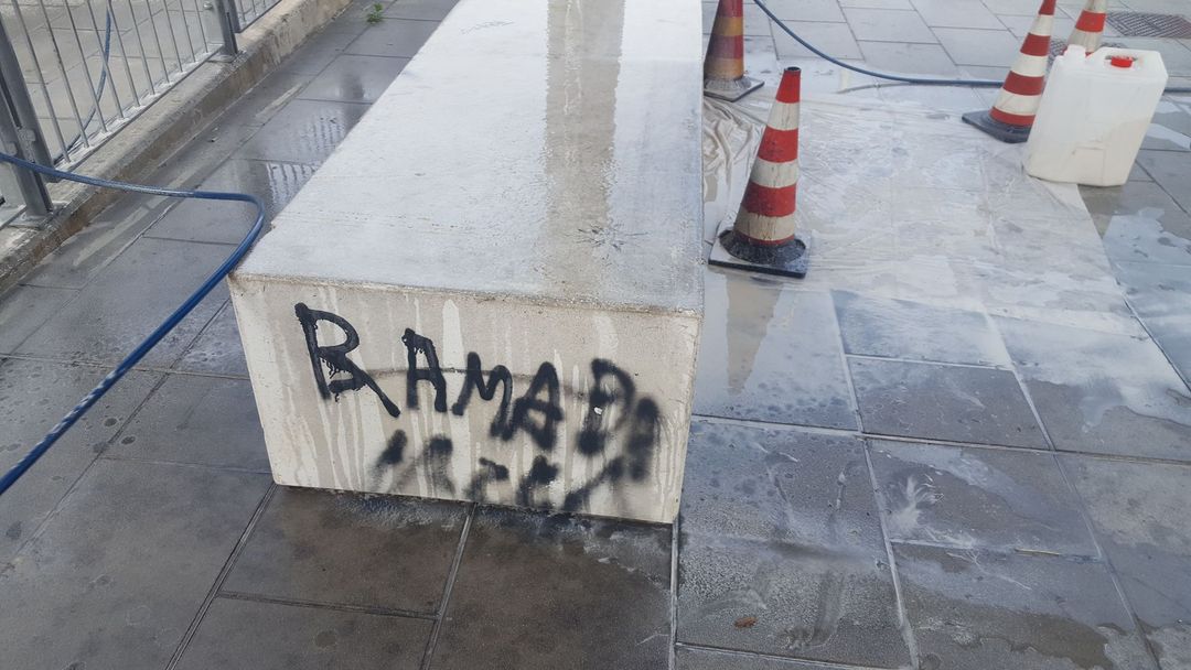 Su un blocco di pietra chiara, in una zona pavimentata, è presente la scritta 