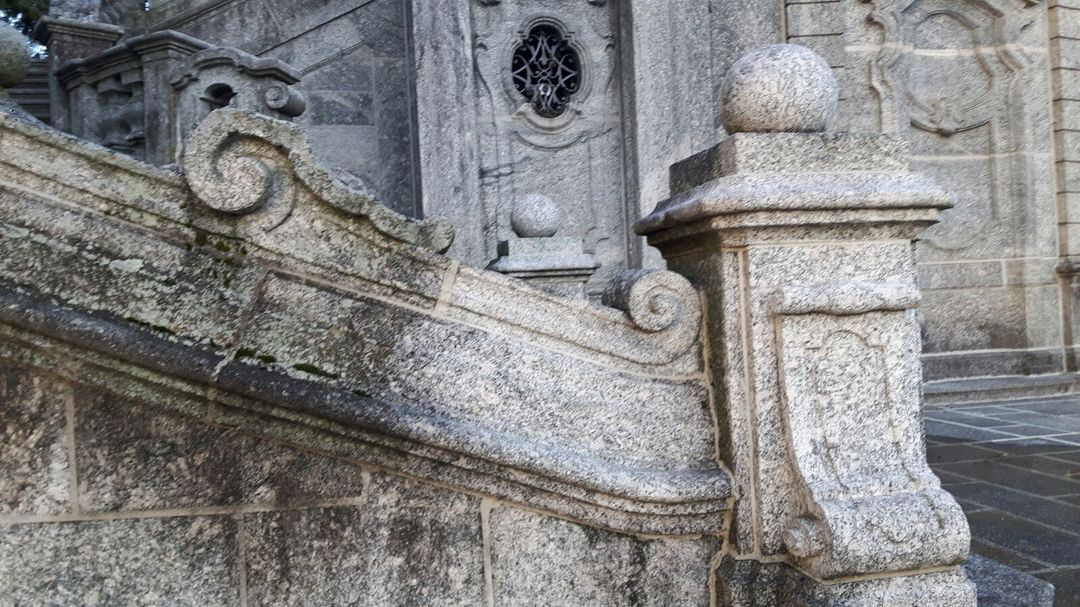 Balaustra in pietra consumata dal tempo e pilastro decorativo di un edificio storico con intagli elaborati.