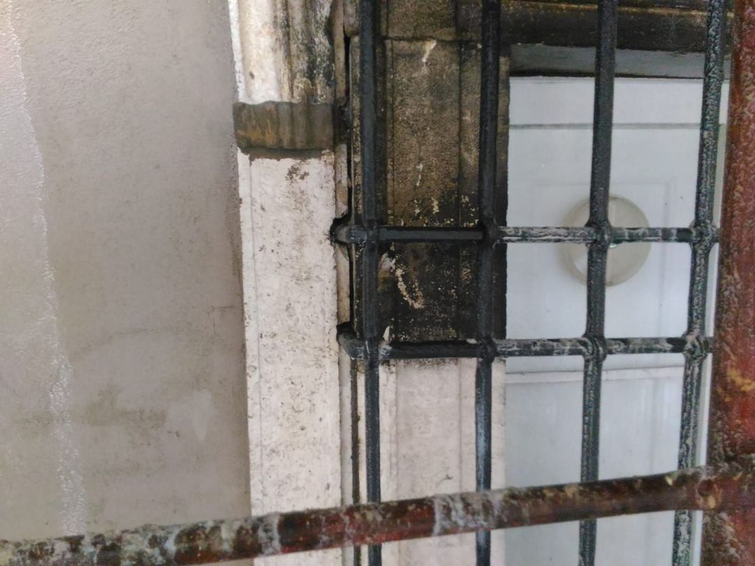 Primo piano di una grata di sicurezza in metallo nero montata su un muro di pietra, con una porta a pannelli bianchi visibile dietro di essa.