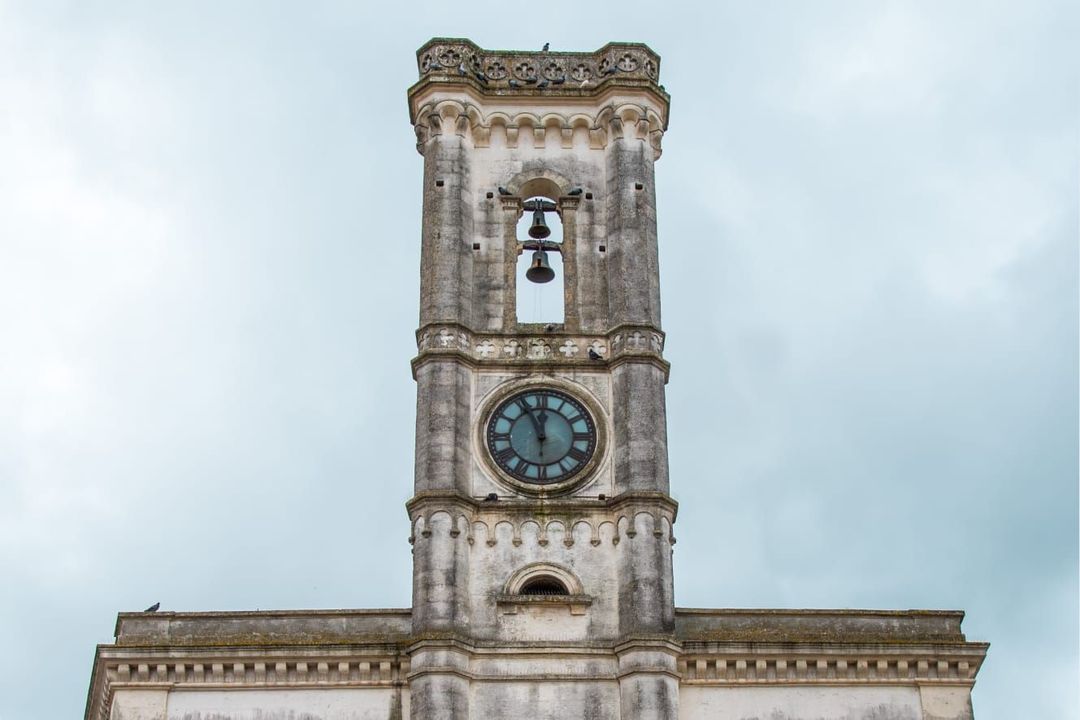 Un campanile in pietra consumato dal tempo con un quadrante di orologio sotto un cielo nuvoloso.