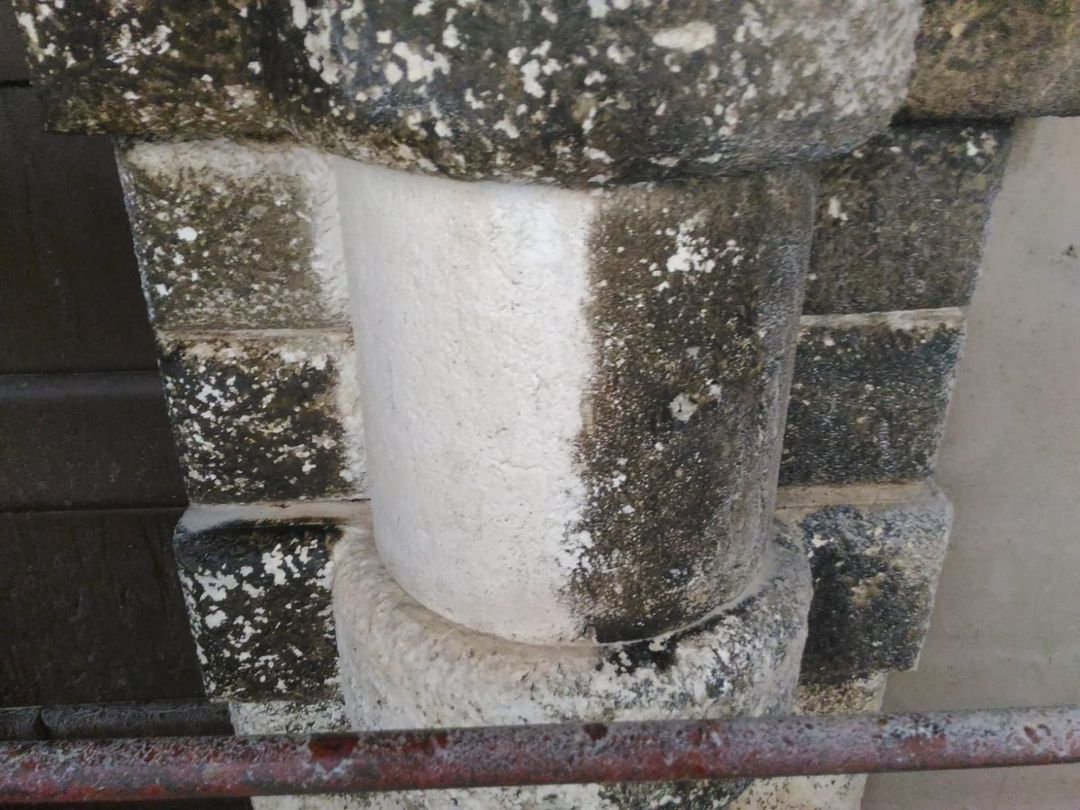 Una colonna di pietra mostrata a metà della pulizia, con il lato sinistro di un bianco brillante e il lato destro ricoperto da uno sporco scuro e invecchiato.