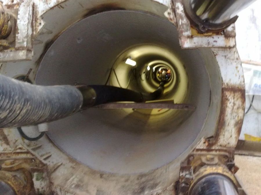 Una ripresa grandangolare degli interni, che mostra un grande tubo industriale dall'alto, con un tubo flessibile scuro che serpeggia verso una luce lontana.