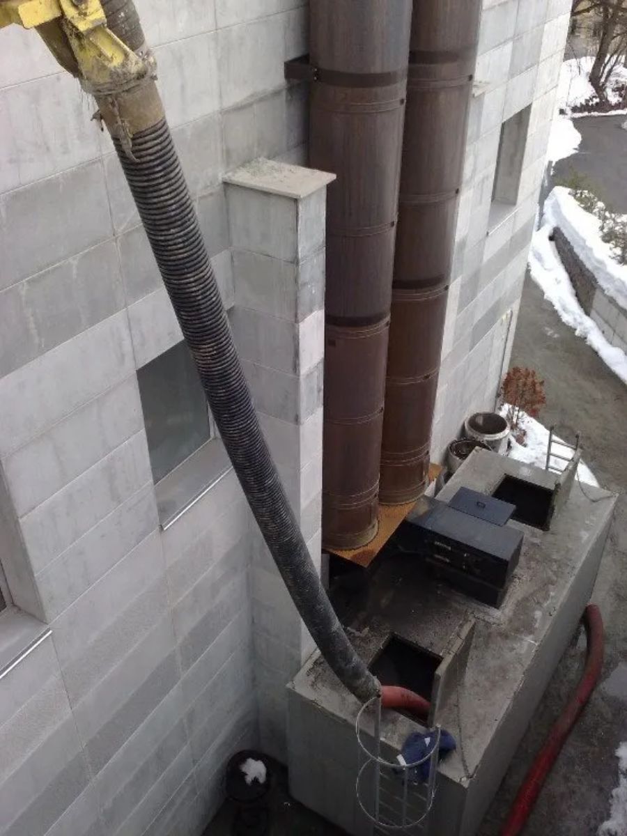 Un lungo tubo flessibile, collegato a un camion non visibile, pompa calcestruzzo in un'apertura sulla sommità di una struttura di servizio in cemento all'esterno di un edificio.