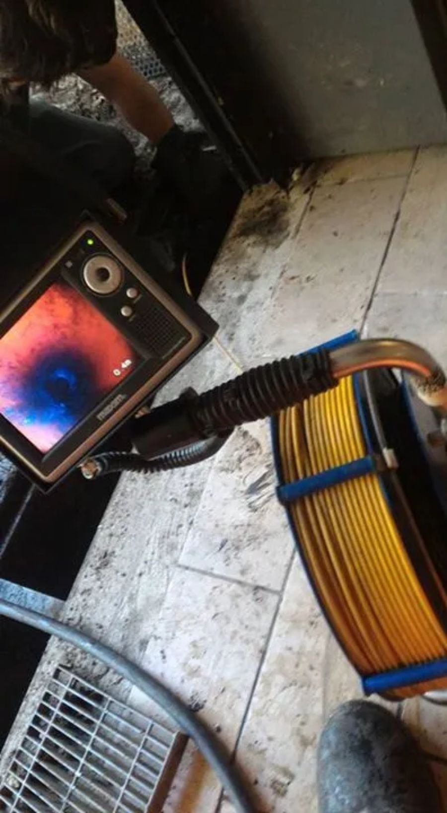 Una telecamera per l'ispezione idraulica mostra un flusso video in diretta su un monitor accanto a un cavo giallo arrotolato su un pavimento piastrellato.