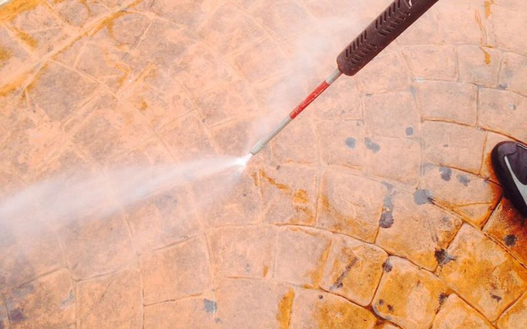 Un'idropulitrice ad alta pressione spruzza acqua su un patio in pietra marrone chiaro e dalla superficie ruvida per pulirlo.