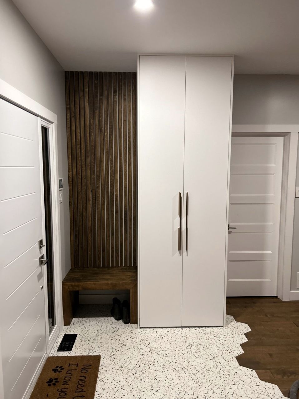 Un couloir avec des armoires blanches, un banc et une porte.