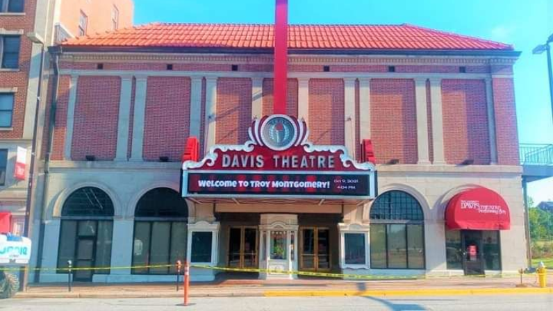 The historic brick Davis Theatre building with a red-tiled roof, marquee, and arched windows on a sunny day.