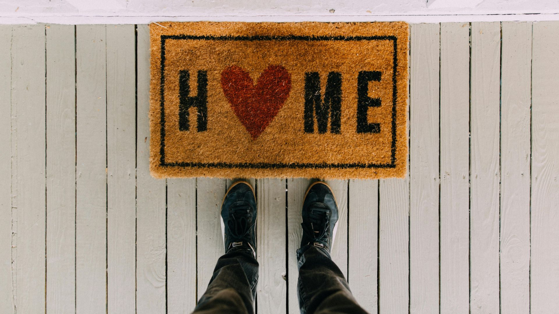 Feet standing on a porch in front of a welcome mat that says 