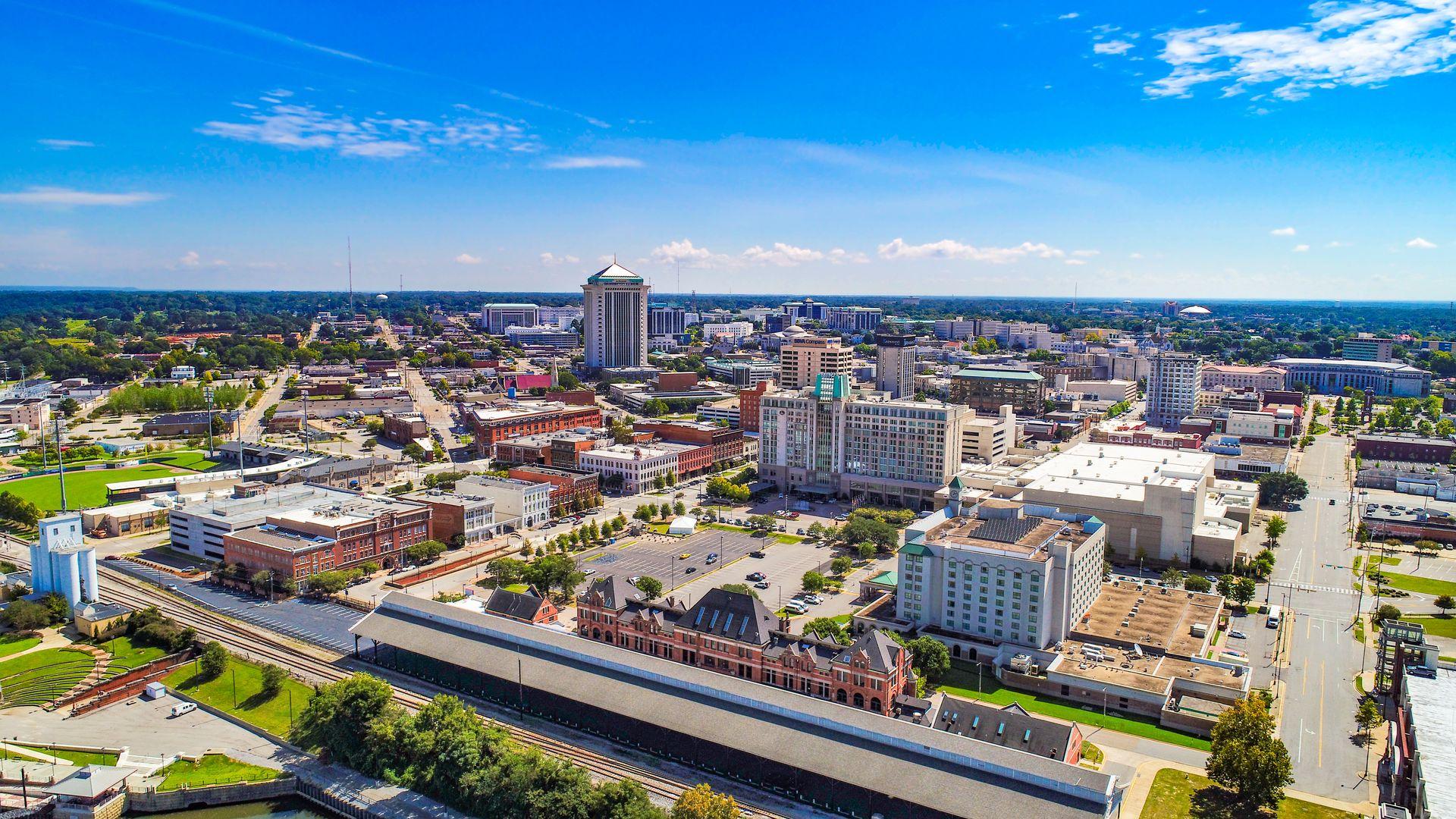 Aerial view of downtown Montgomery, AL, with buildings, green spaces, and a clear blue sky.