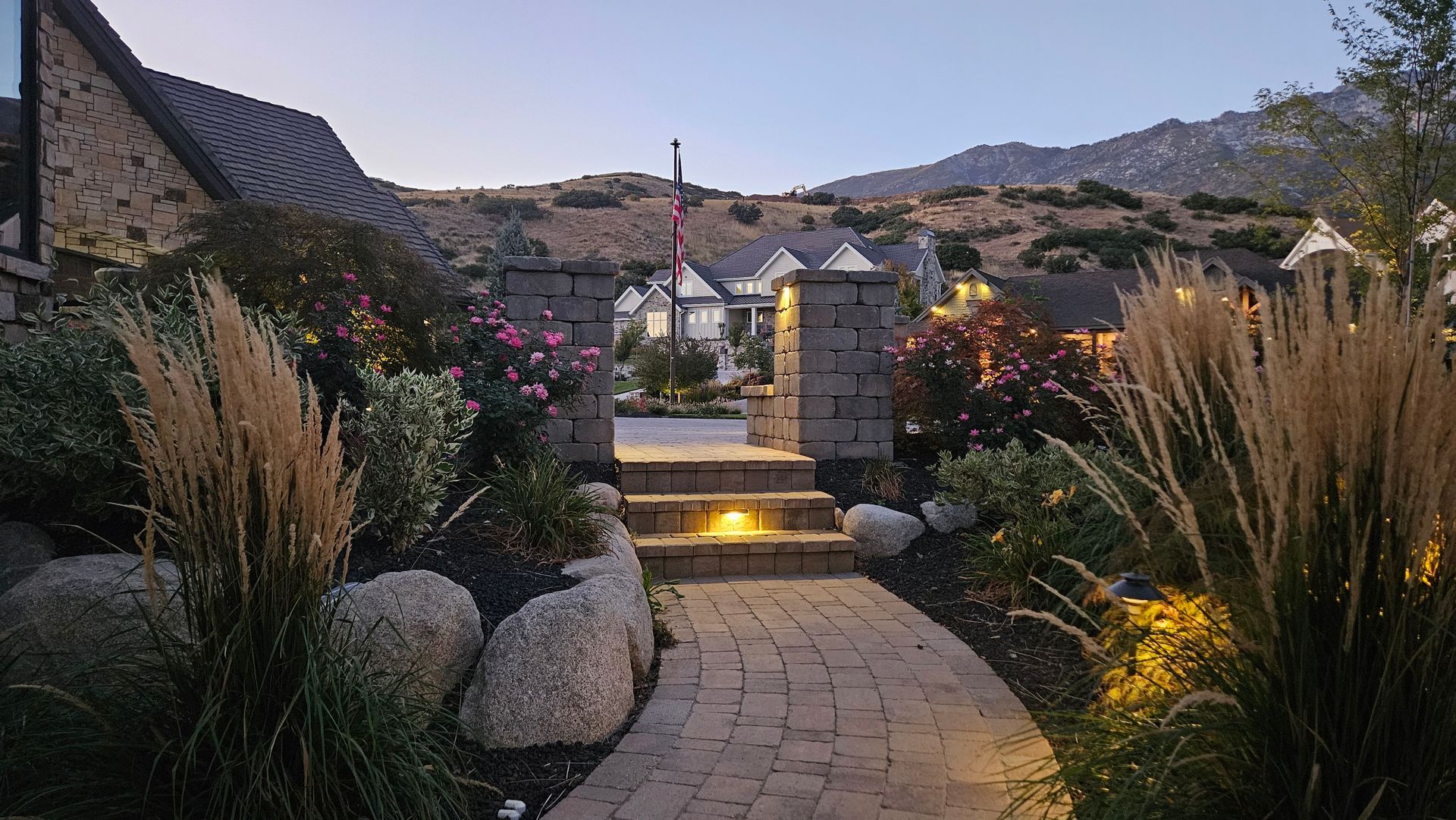 A tiered stone garden with a cascading waterfall, stone steps, and colorful flowers along a landscaped pathway.