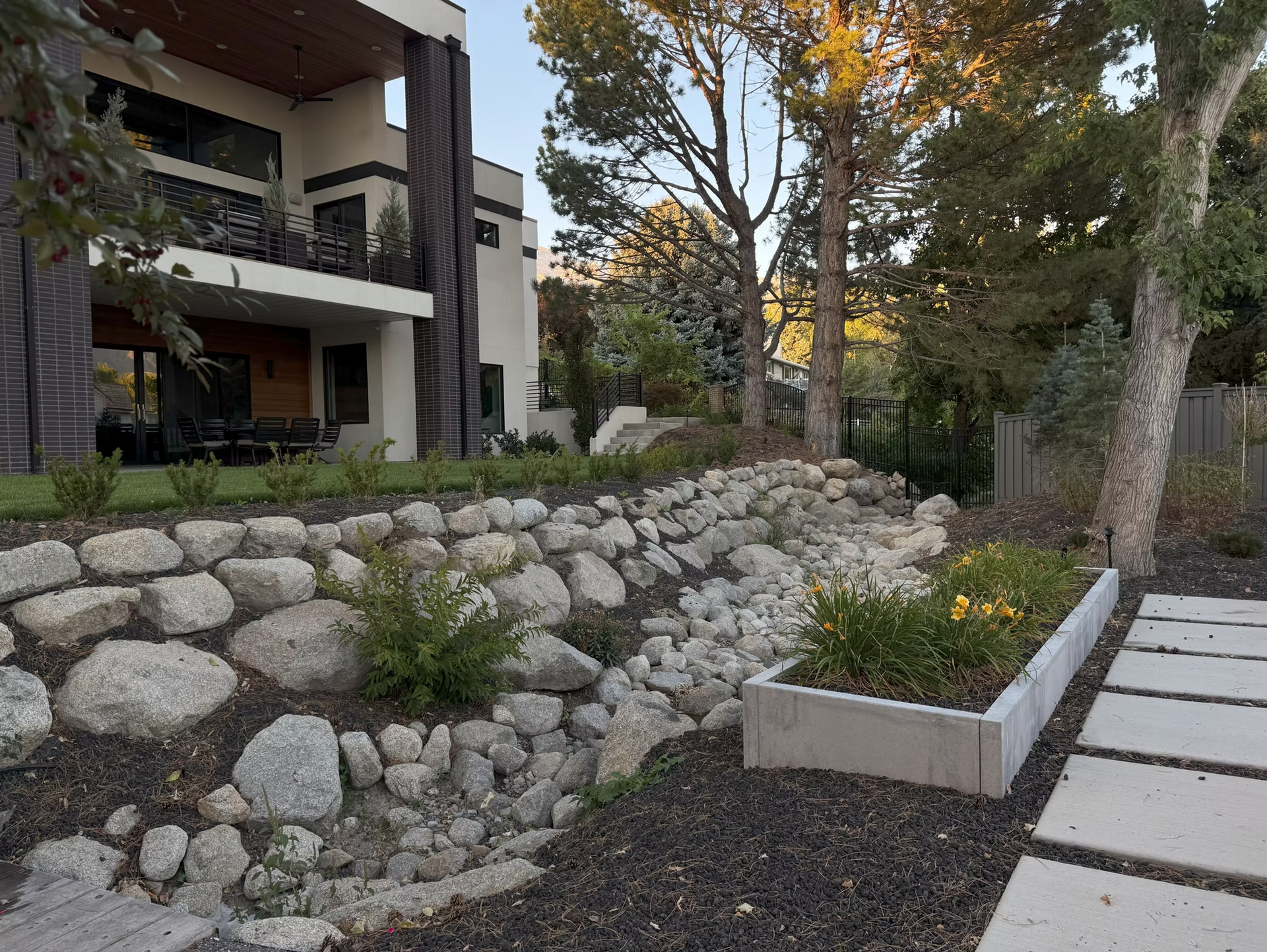 Modern house with a stone retaining wall, terraced landscaping, a concrete planter, and a stone paver pathway.