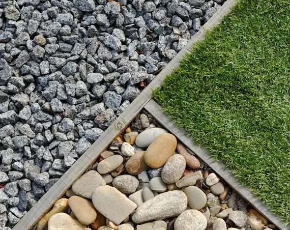 A top-down view showing a garden transition area with angular grey gravel, smooth rounded tan stones, and green grass.