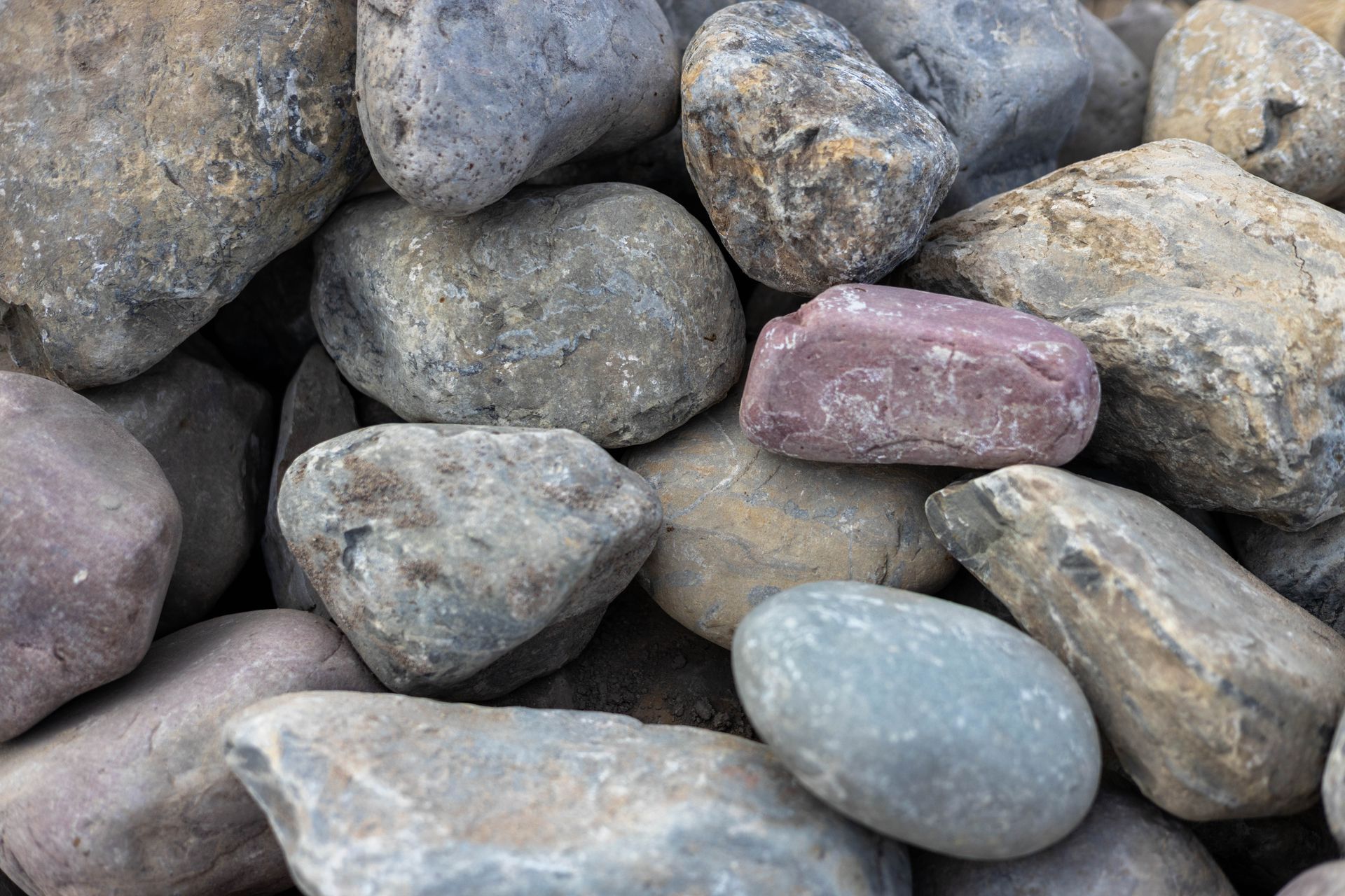 Smooth gray and beige pebbles tightly packed together in a close-up texture pattern
