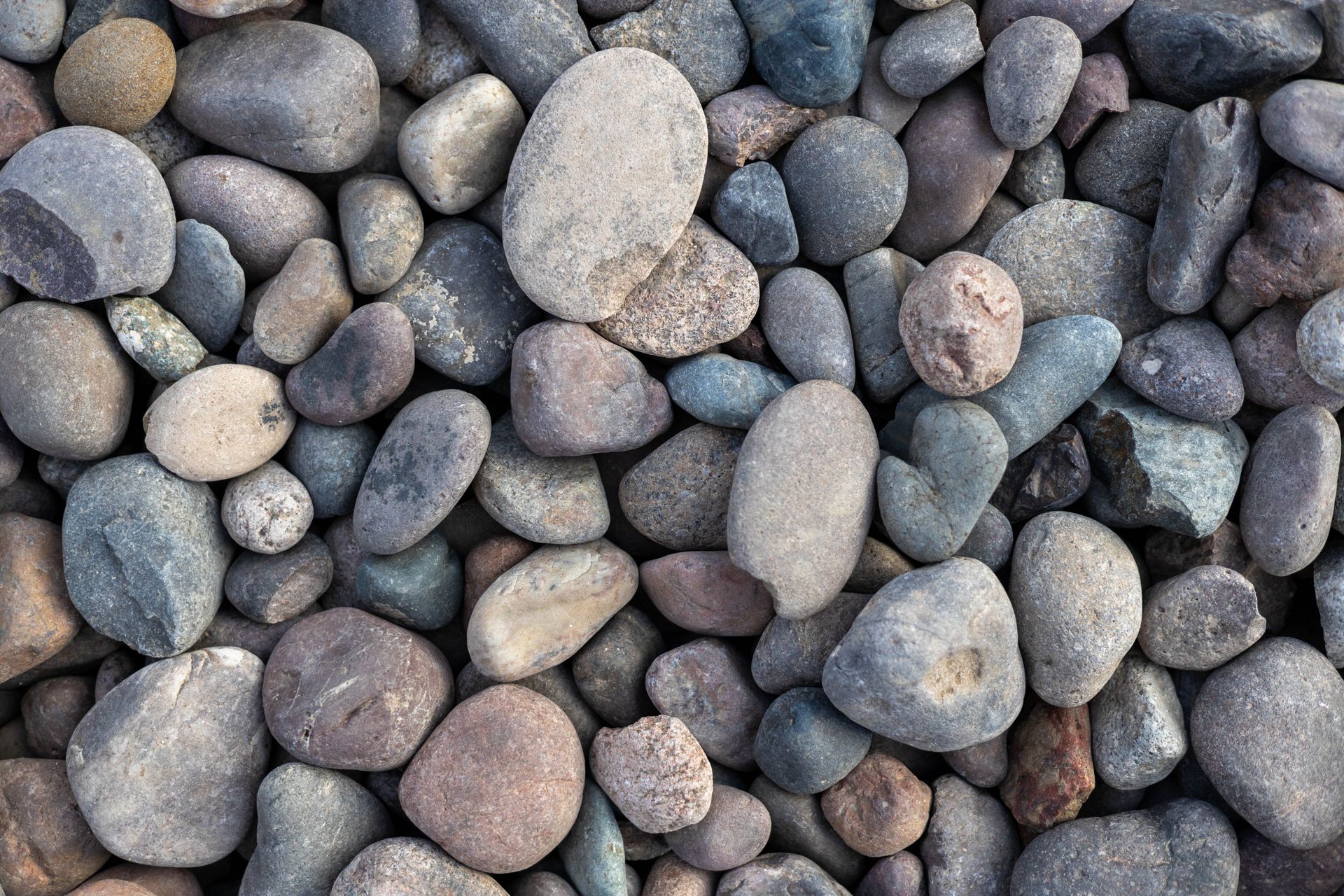 Smooth gray and beige pebbles tightly packed together in a close-up texture pattern