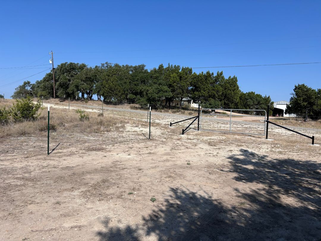 A dirt field with a fence and trees in the background.