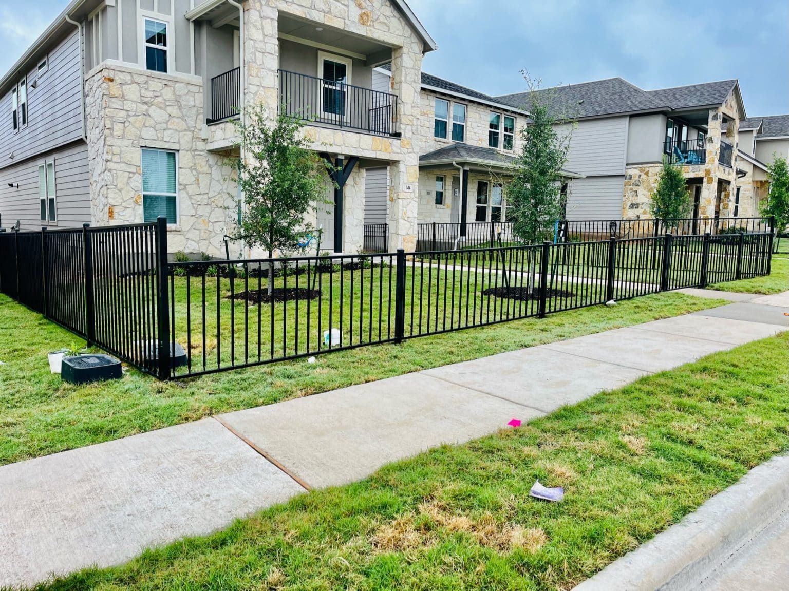 A black fence surrounds a lush green yard in front of a house.