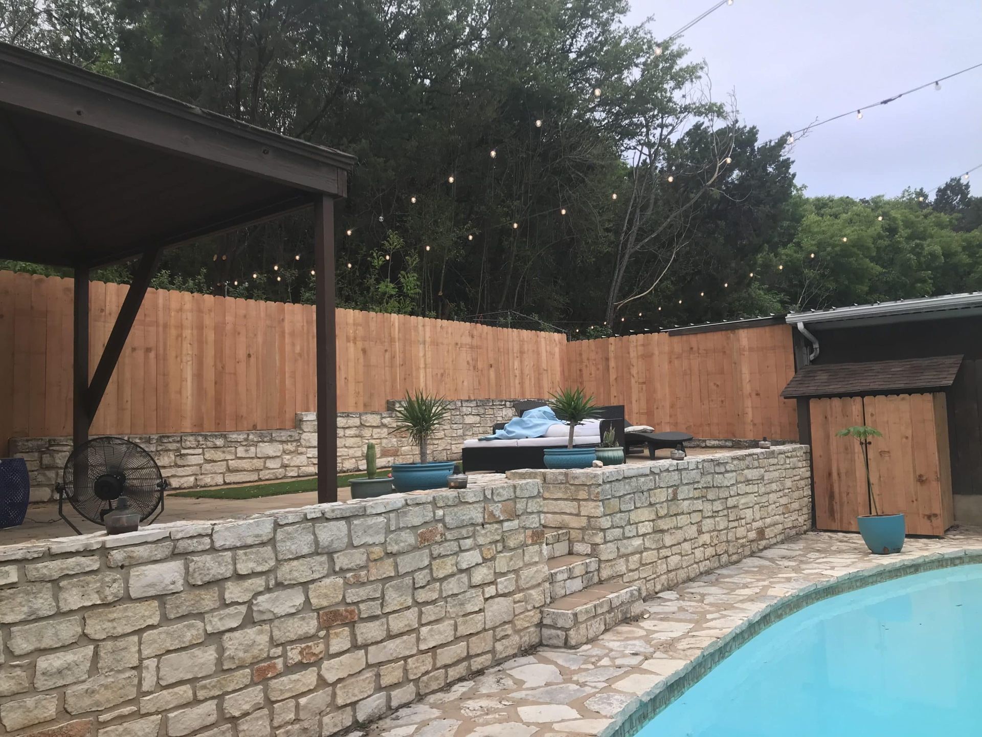 A wooden fence surrounds a swimming pool in a backyard.