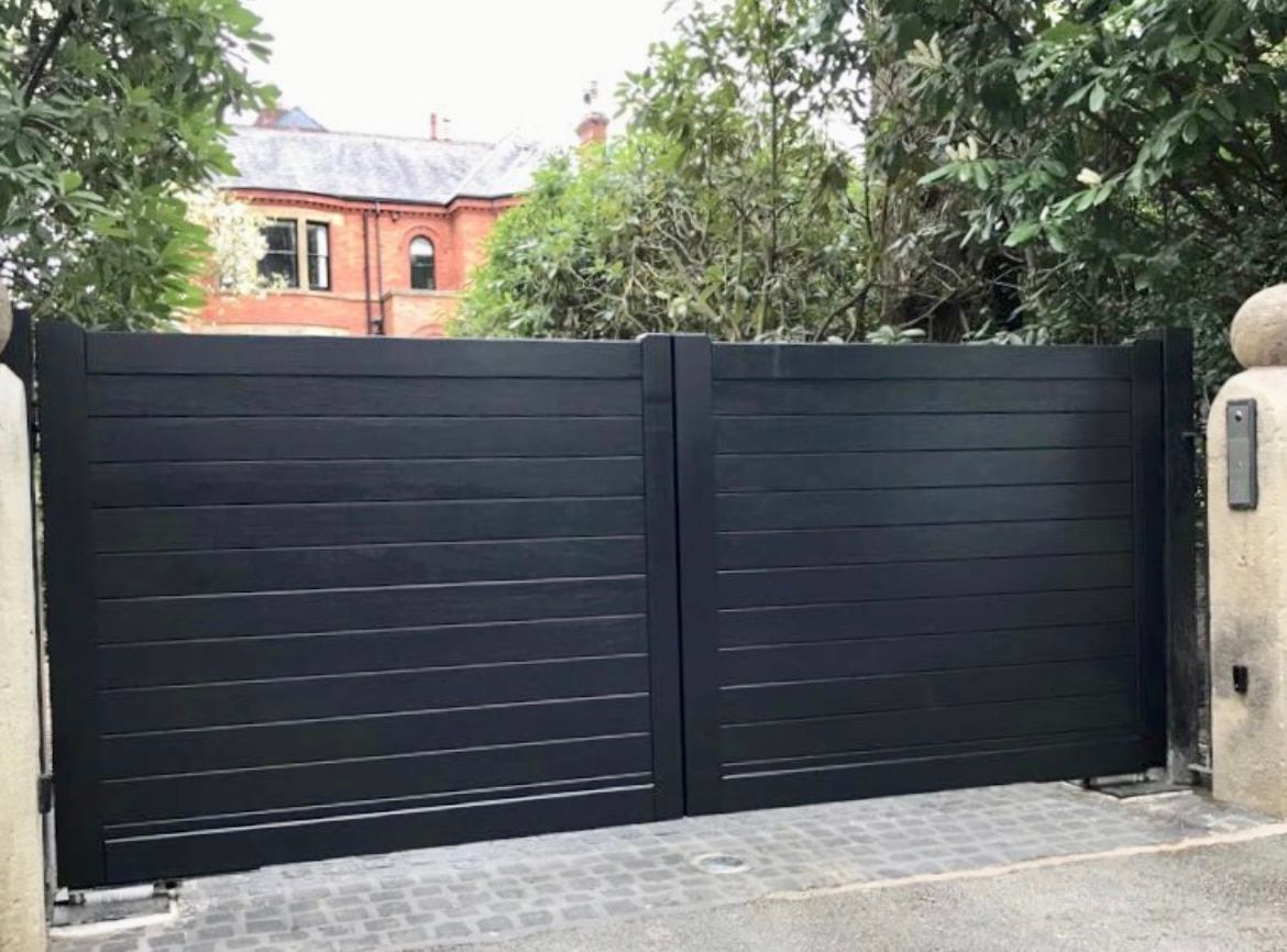 A black gate is open to a driveway in front of a house.