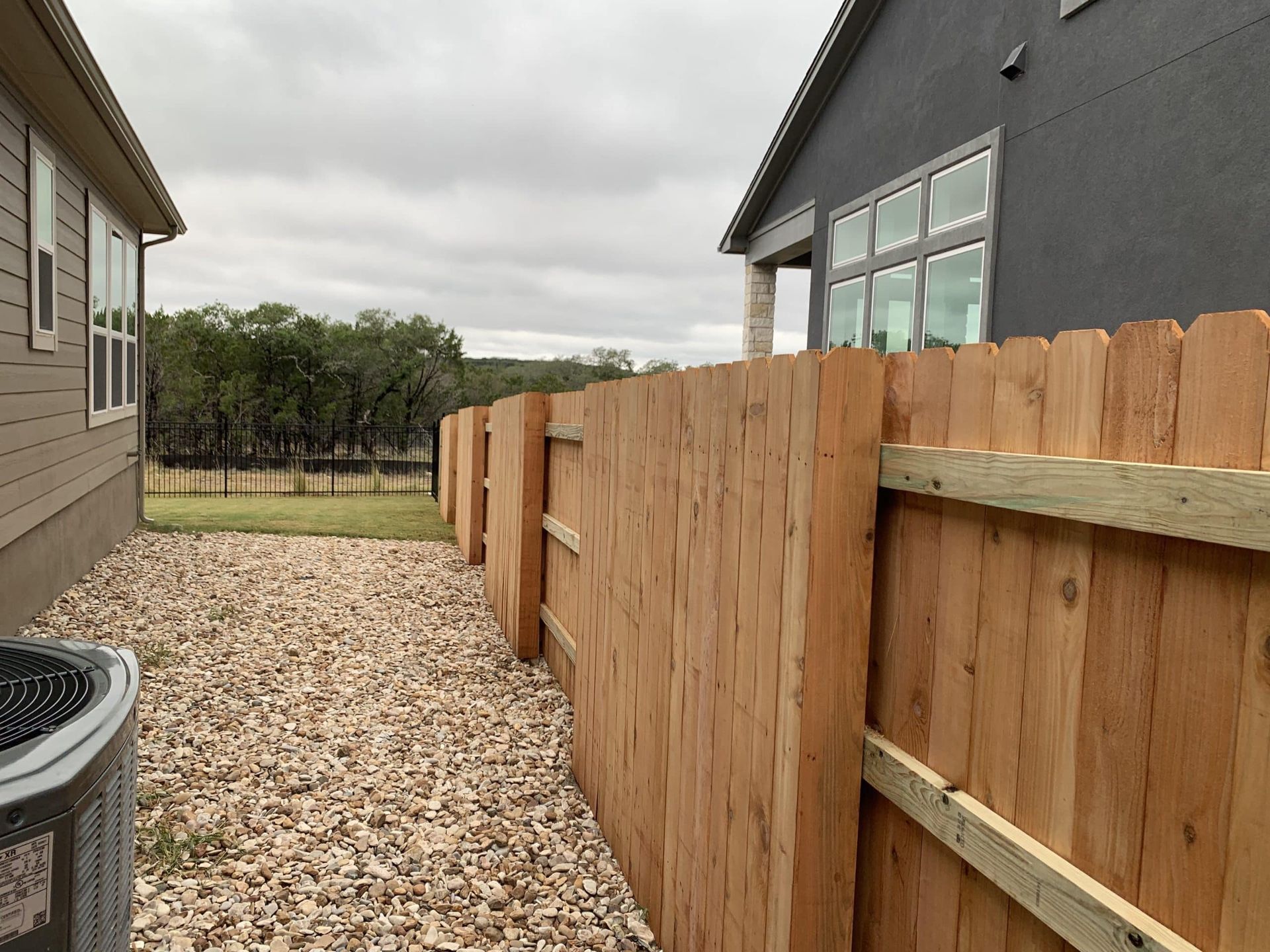 Wooden fence separating two houses; gravel ground; cloudy sky.