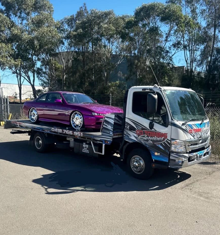 Purple Car Loaded on A Tow Truck, Parked on A Paved Lot on A Sunny Day — Cq Towing Services In Rockhampton City, QLD