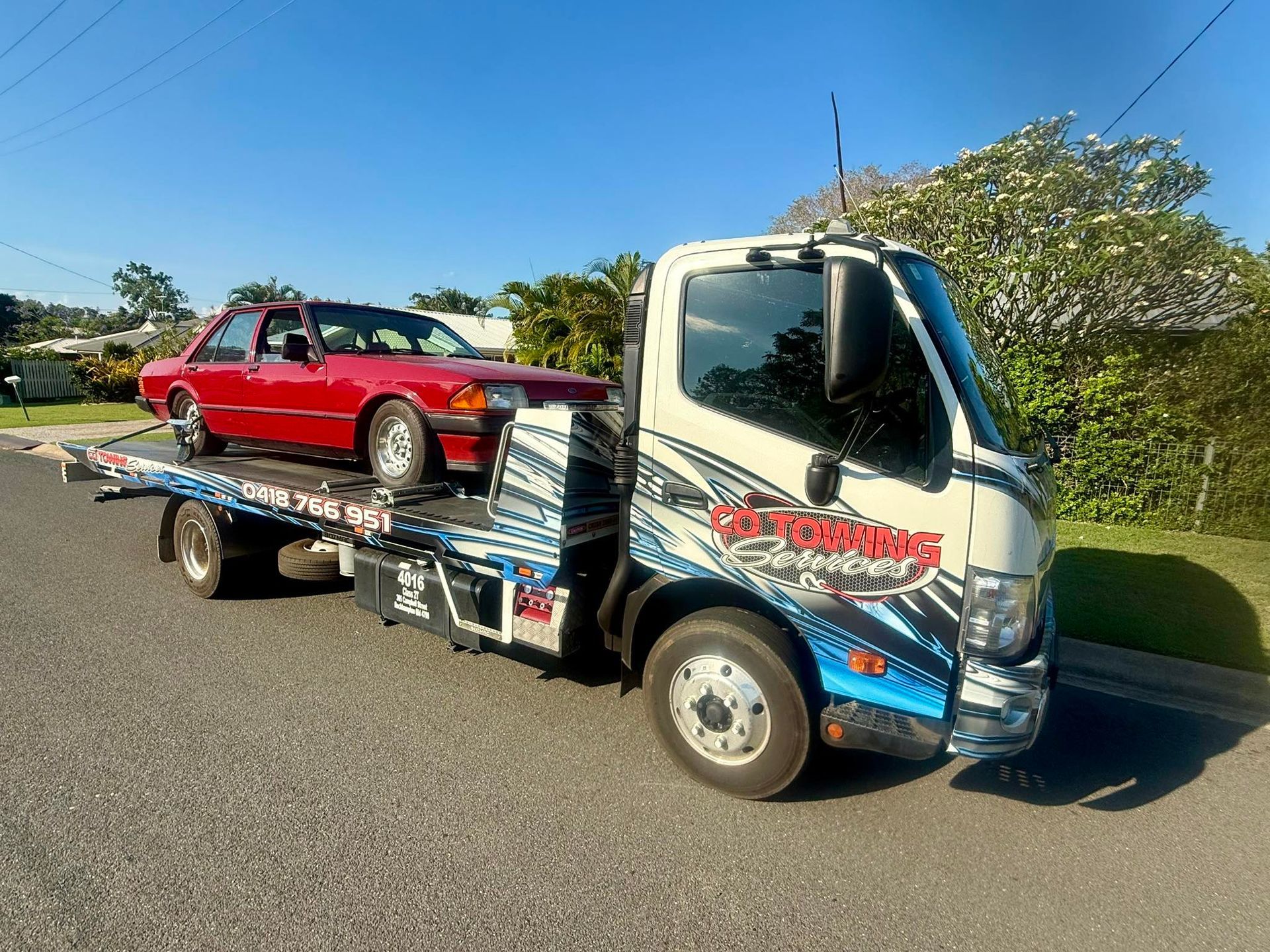 Tow truck with red car on a sunny day. The truck has blue and white graphics.