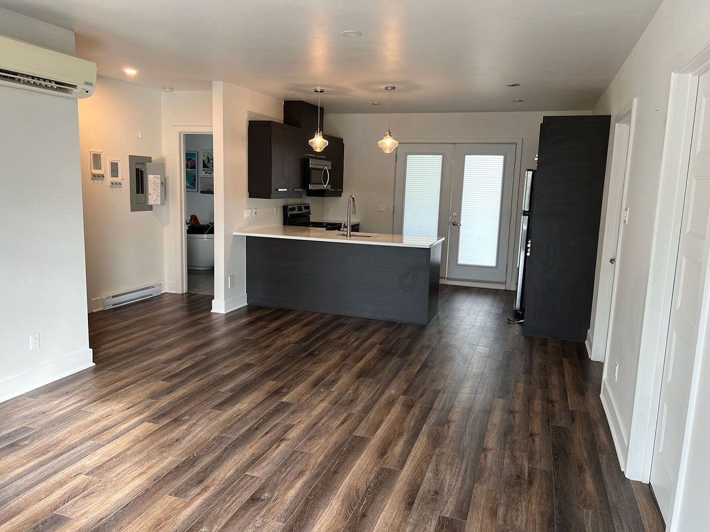 Un salon avec parquet et une cuisine en arrière plan.