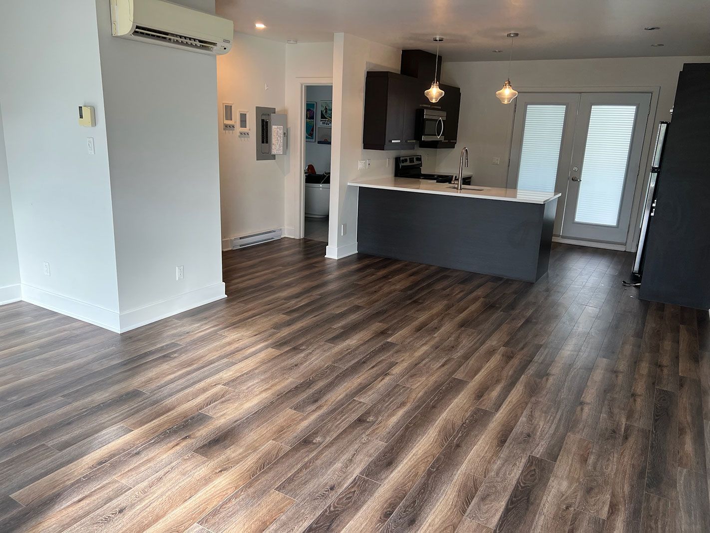 Un salon avec parquet et une cuisine en arrière plan.