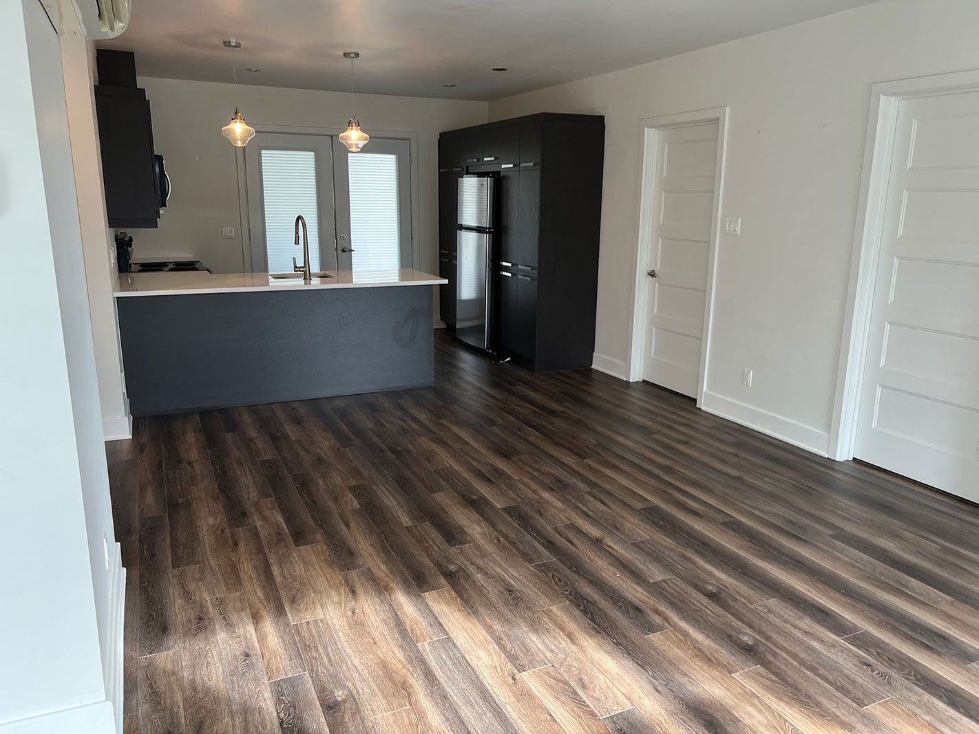 Un salon avec parquet et une cuisine en arrière plan.