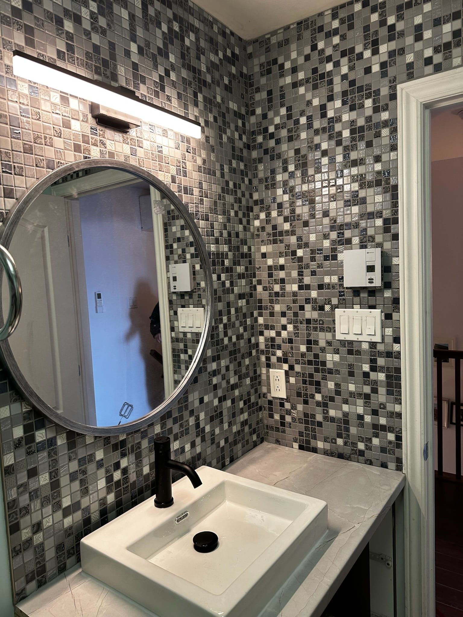 Une salle de bain avec lavabo, miroir et mur en mosaïque.
