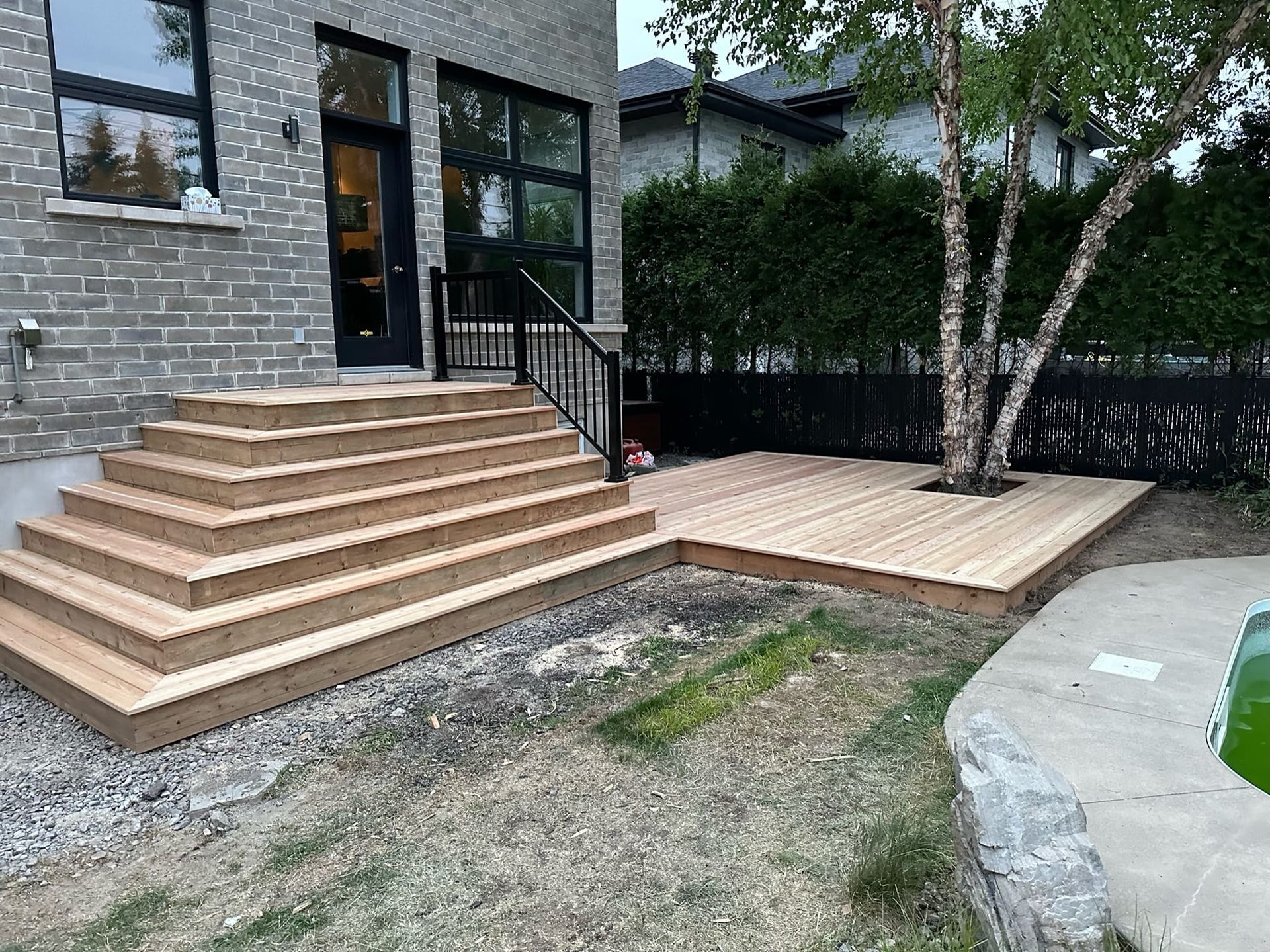Une terrasse en bois avec des escaliers qui y mènent devant une maison en briques.